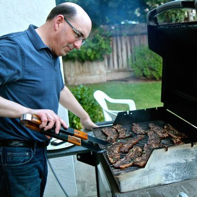Man grilling steak outdoors on a barbecue grill in a backyard setting.