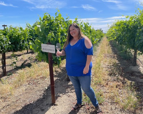 Woman in blue shirt holding wine glass at Aguianico vineyard in Lodi, California.