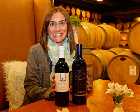 Woman holding two bottles of wine at Lodi Winegrape Commission tasting event in a winery cellar.
