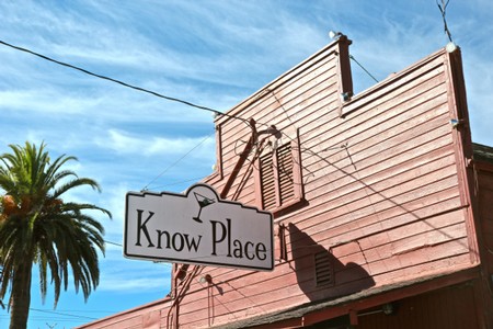 Historic Know Place building with a pink facade and a sign, under a blue sky with palm trees nearby.