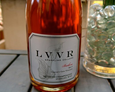 Lodi Winegrape Commission sparkling wine bottle with a white label and a glass of ice in the background.