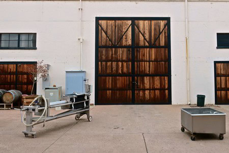 Wine production equipment outside a winery with large wooden doors in Lodi, California.