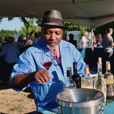 Man tasting wine at Lodi Winegrape Commission outdoor event with bottles and glasses.