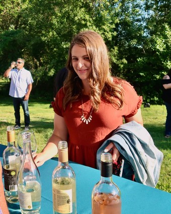 Young woman at Lodi Winegrape Commission outdoor event with wine bottles and greenery.