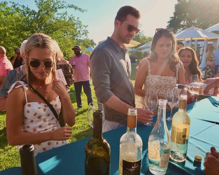 People enjoying wine tasting at an outdoor event with wine bottles on a table.