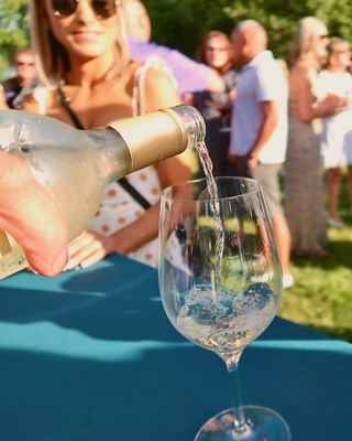 Person pouring wine into a glass at a Lodi Winegrape Commission event outdoors.