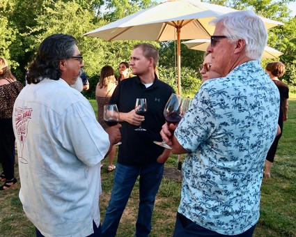 People enjoying wine tasting outdoors at a Lodi Winegrape Commission event with trees and umbrellas in the background.