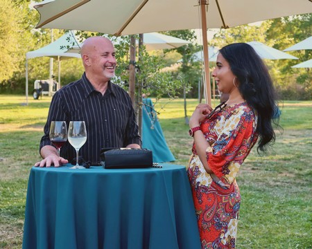 Two people enjoying a conversation at an outdoor wine tasting event with wine glasses and umbrellas.