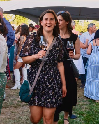 Women enjoying wine tasting at Lodi Winegrape Commission outdoor event with crowd and tents.
