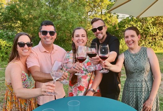 Group of friends celebrating with wine outdoors in a sunny garden setting.