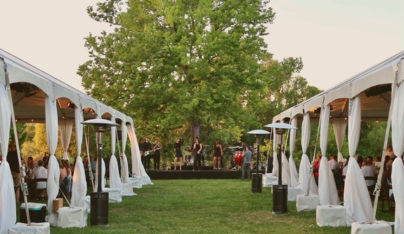 Outdoor event organized by Lodi Winegrape Commission with tents, stage, and audience in a lush green setting.