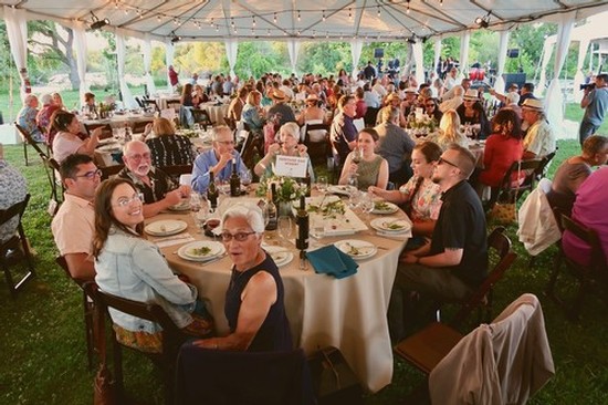 Large outdoor gathering under a tent with people enjoying a meal at a community event.