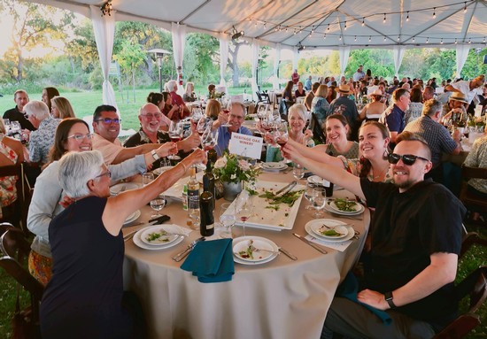 Group of people enjoying a toast at an outdoor event under a tent, celebrating wine and community.