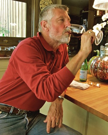 Man tasting red wine in a cozy winery setting with wine bottles and flowers nearby.