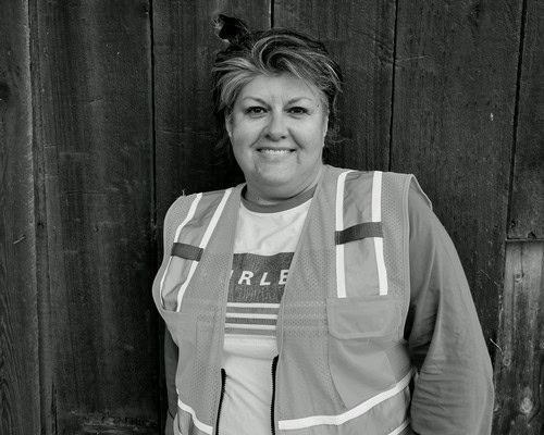 Black and white photo of a woman in a safety vest standing in front of a wooden fence.
