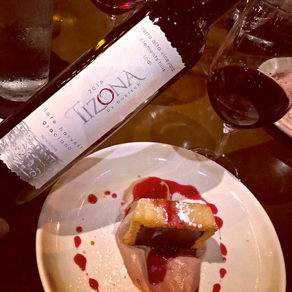 A glass of red wine, a bottle of Lodi wine, and a dessert with red sauce on a white plate.