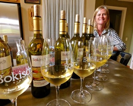 Woman enjoying wine tasting with bottles of wine from Lodi Winegrape Commission on table.