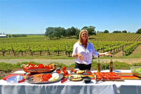 Woman presenting fresh vineyard produce and wine bottles at Lodi Winegrape Commission event.