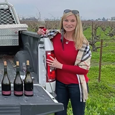 Woman in vineyard with wine bottles, showcasing Lodi winegrapes and wine production.