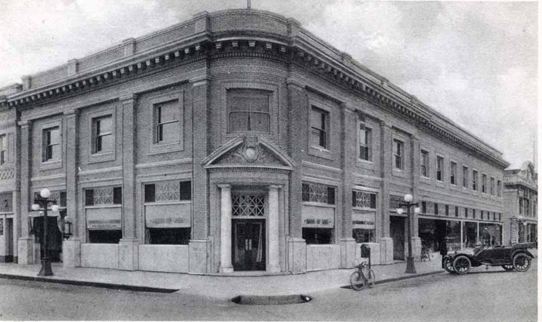 Black and white photo of the historic Lodi Winegrape Commission building with vintage cars and bicycles outside.