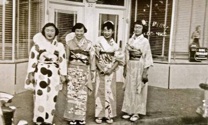 Four women in traditional Japanese kimonos standing outside a building in a vintage photo.