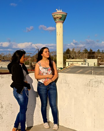 Two women standing on a rooftop with the Lodi water tower in the background.