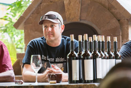 Man tasting wine at Lodi Winegrape Commission event with wine bottles and glasses on table.