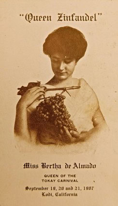 Vintage poster of Queen Zinfandel with woman holding grapes and a sword, promoting Lodi wine event 1927.