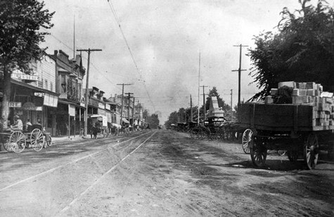 Vintage black and white photo of Lodi's main street with old storefronts and horse-drawn wagons.