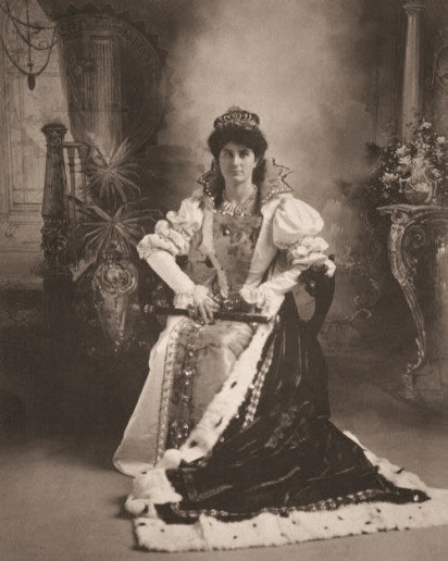 Sepia-toned portrait of a woman in Victorian dress with elaborate accessories, seated in an ornate setting.