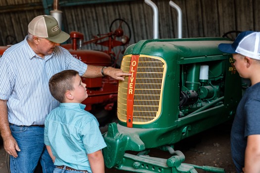 Man and children examining a vintage green Oliver tractor at the Lodi Winegrape Commission event.