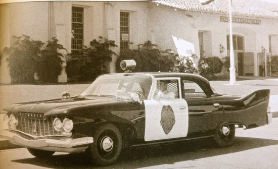 Black and white vintage police car with a badge emblem on the door, parked on a street in Lodi, California.