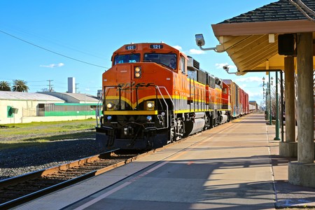 Orange freight train at Lodi train station with clear blue sky and station platform.