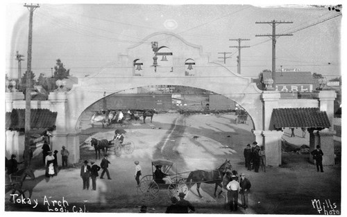Black and white photo of Tokay Arch in Lodi, California, with people, horses, and street scene from early 20th century.