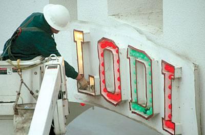 Worker installing illuminated Lodi Winegrape Commission sign on building exterior for branding and promotion.