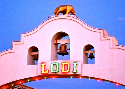 Lodi Winegrape Commission sign with colorful lights and a bell tower against a blue sky.
