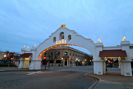 Historic Lodi Winegrape Commission gateway with illuminated arch and surrounding buildings at dusk.