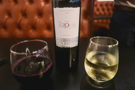 Two glasses of wine, red and white, with a bottle of Tizona wine on a dark table.