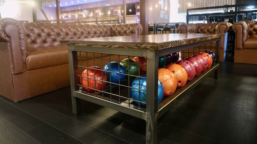 Colorful bowling balls on a rack in a modern bowling alley with leather couches in the background.