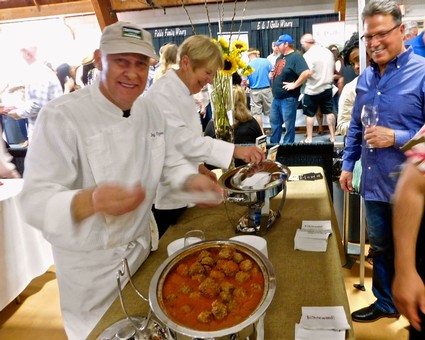 Chef serving wine and food at Lodi Winegrape Commission event with guests in background.