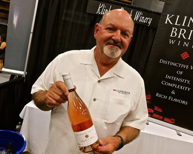 Man holding a bottle of rosé wine at a wine tasting event, smiling at the camera.