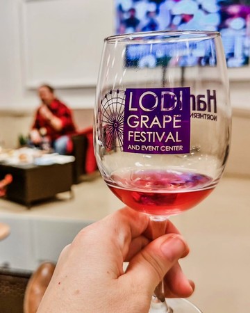 Glass of red wine at Lodi Winegrape Festival with event center in background.