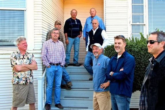 Group of nine men standing on steps outside a house, smiling and posing for a photo, representing Lodi Winegrape Commission.