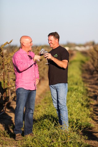 Two men enjoying wine tasting in a vineyard, celebrating success and camaraderie.