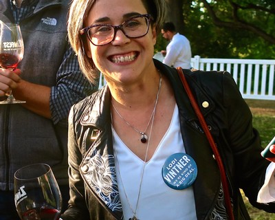 Smiling woman with glasses at Lodi Winegrape Commission event, wearing a badge and black leather jacket.