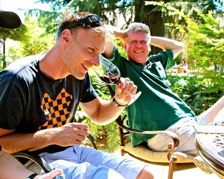 Two men enjoying wine outdoors at a Lodi Winegrape Commission event in a lush green setting.
