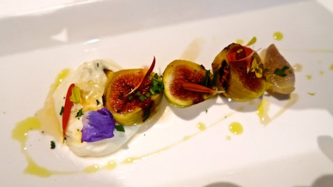 Gourmet dish featuring fresh figs, herbs, and edible flowers on a white plate, highlighting Lodi wine region cuisine.