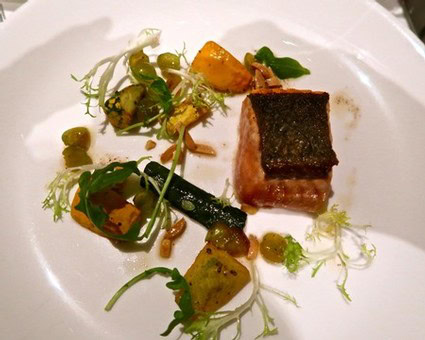 Elegant gourmet dish featuring seared fish, assorted vegetables, and microgreens on a white plate.