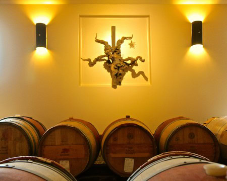 Wine barrels in a cellar with warm lighting and a decorative wall art piece.