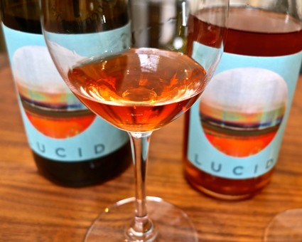Glass of rosé wine with bottles in the background, showcasing Lodi Winegrape Commission branding.